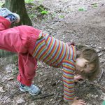 Ein Kind in bunt-gestreifter Kleidung versucht am Waldboden einen Handstand zu machen