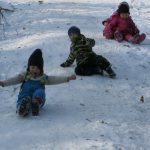 Kinder rutschen auf dem Schnee einen Hang hinunter