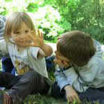 Drei Kinder unterhalten sich sitzend am Waldboden